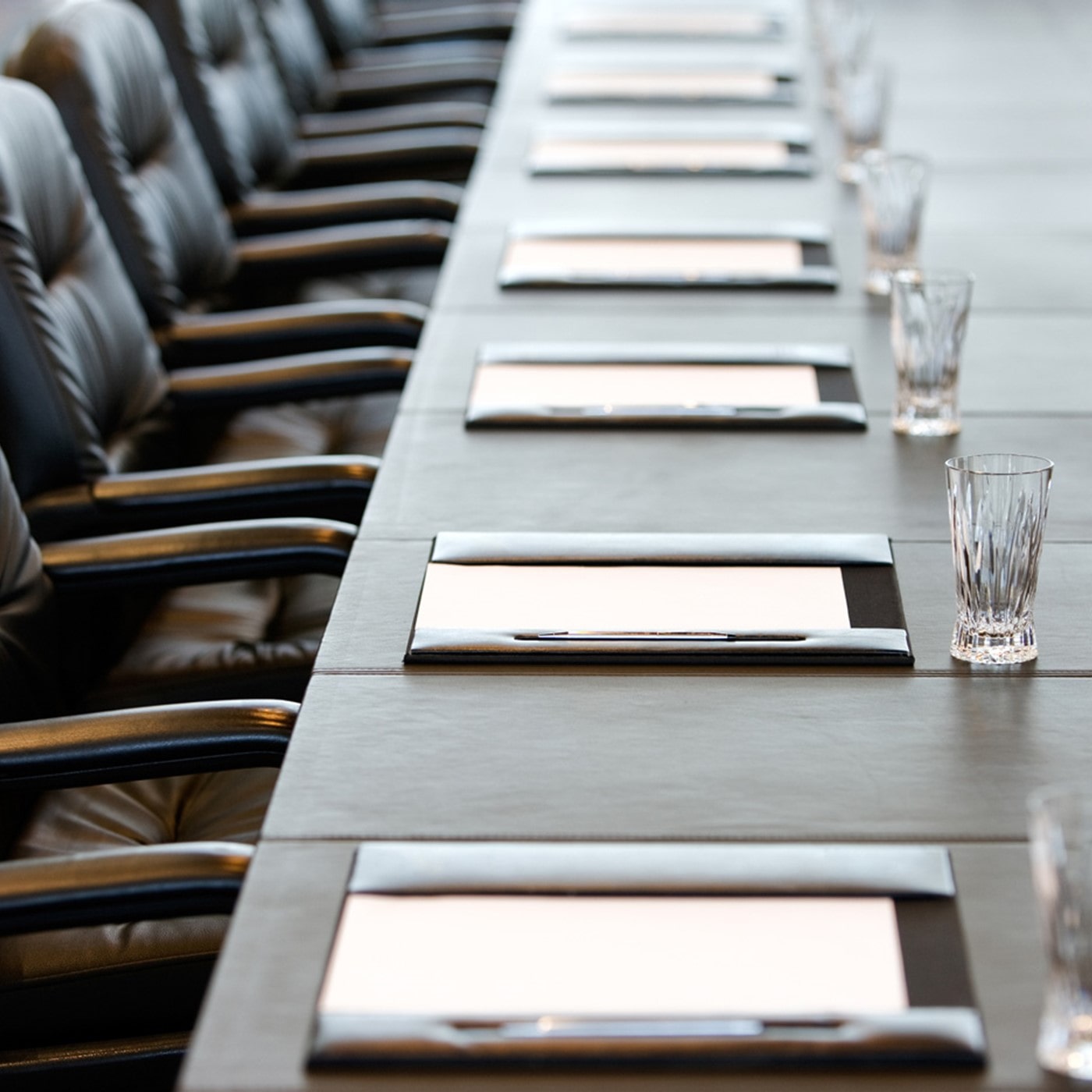 A long table set up for a board of directors meeting, with leather chairs, neatly placed notepads, pens, and water glasses, suggesting a formal and organized corporate environment.