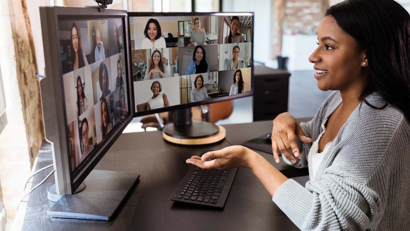 A person at a desk gesturing towards a computer monitor displaying multiple video conference participants, illustrating the importance of virtual meetings in remote work and digital communication.