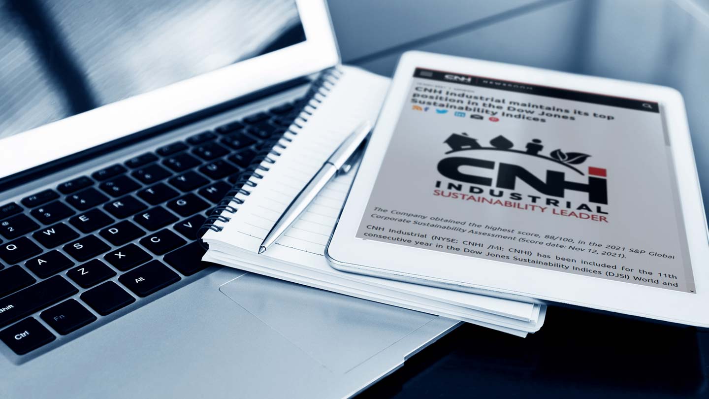 A close-up of a tablet displaying ‘CNH Industrial Sustainability Leader’ on a desk with an open laptop, notebook, and pen, emphasizing sustainability in industrial practices within a professional setting.